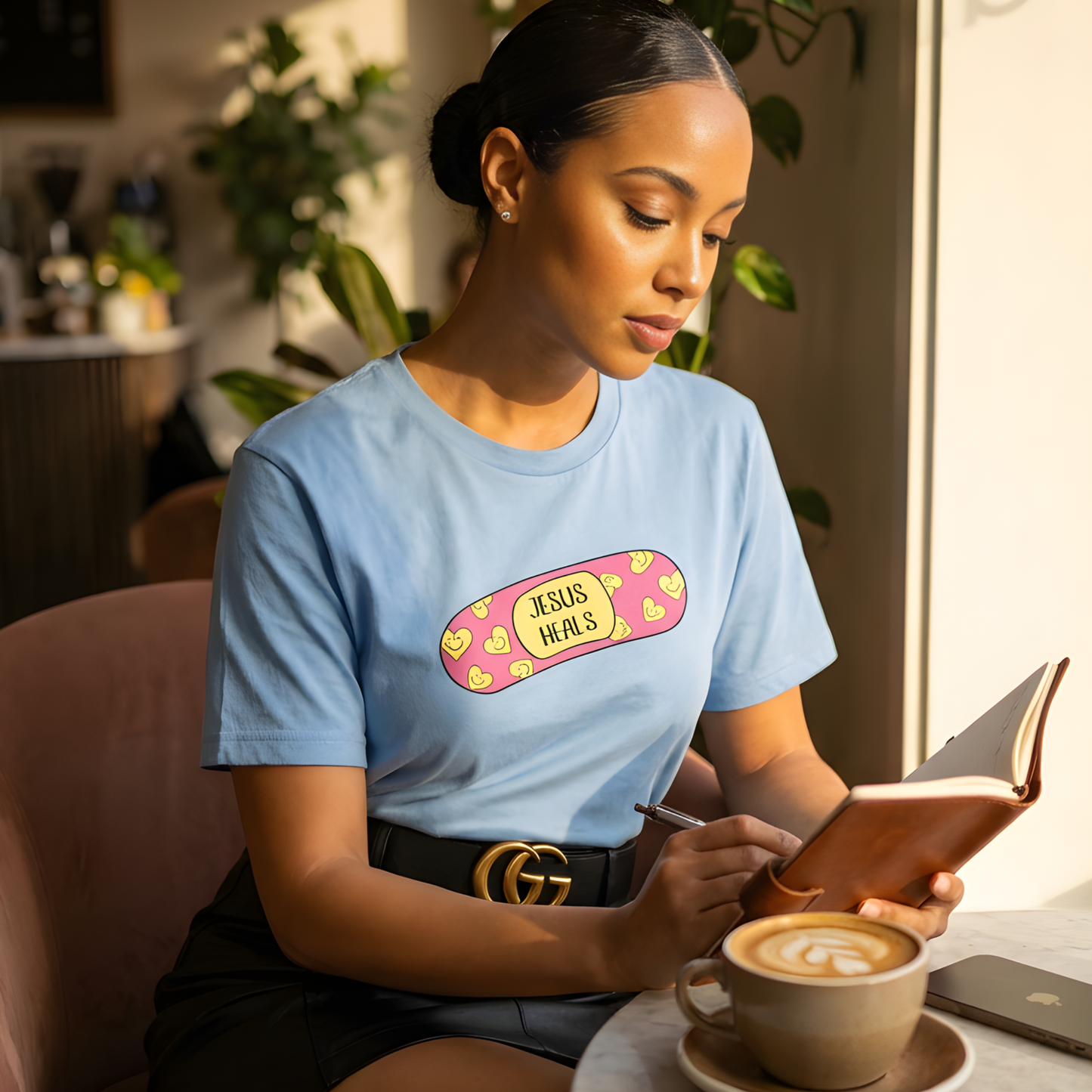 Woman wearing a blue t-shirt with a graphic design, sitting at a table with a cup of coffee and a book.